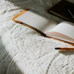 An open book sitting on top of a bed next to a pencil